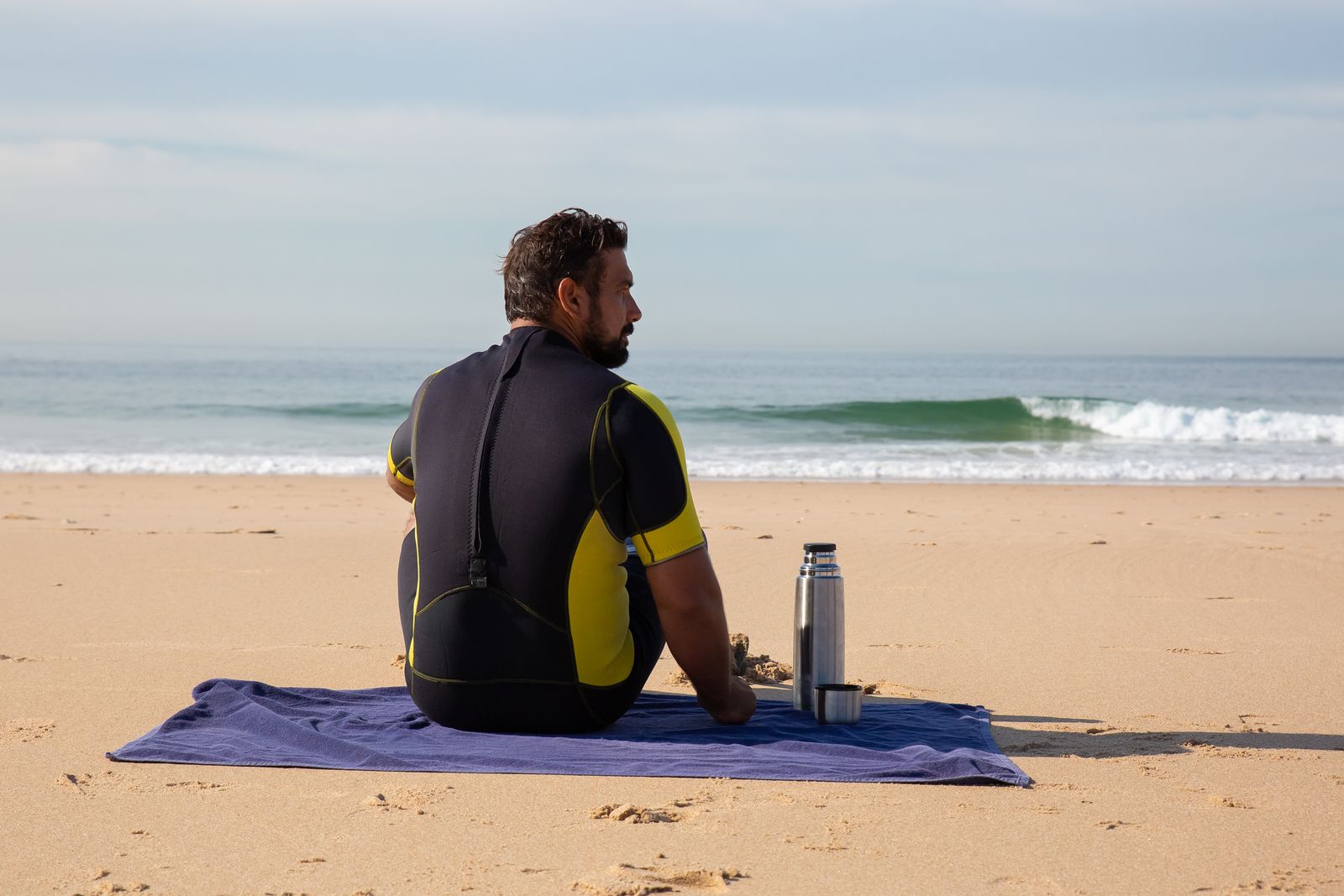A swimmer on the bank wrapped in warm layers with a hot drink after a cold dip